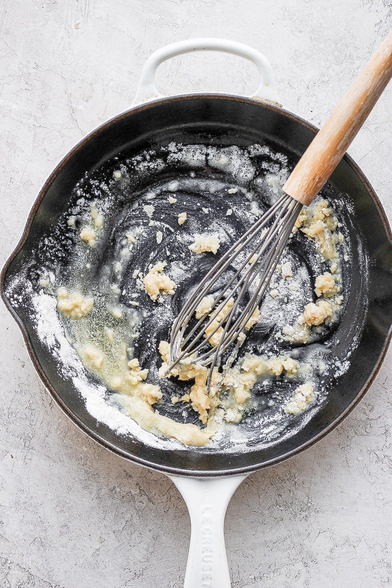 Cast iron skillet with a roux inside and whisk sticking out. 