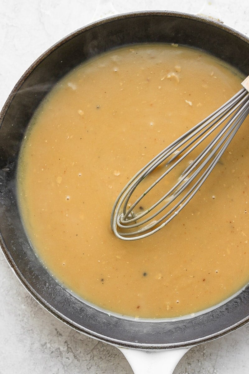 Cast iron skillet filled with gravy with a whisk sitting in it. 