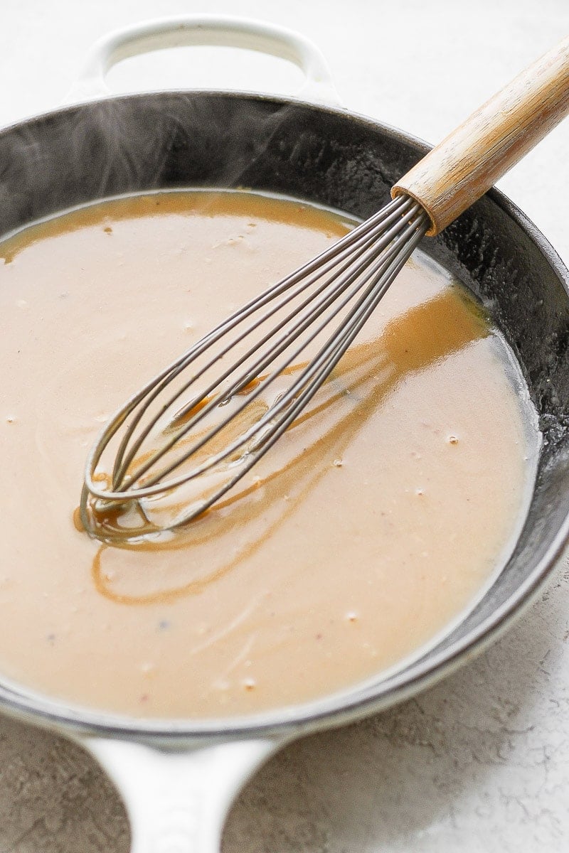 Cast iron skillet filled with gravy with a whisk sitting in it. 