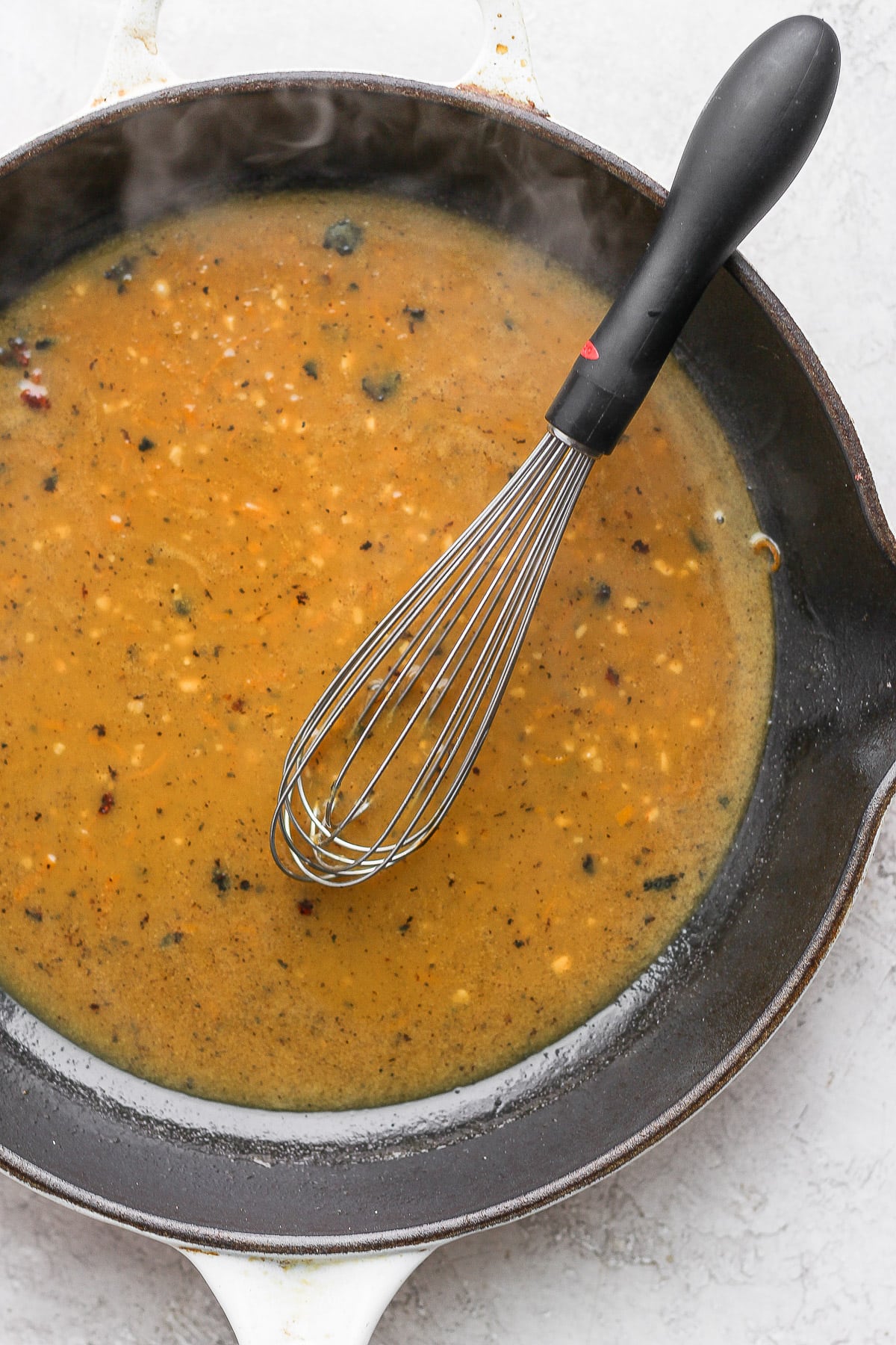 Skillet with orange chicken sauce and a whisk. 