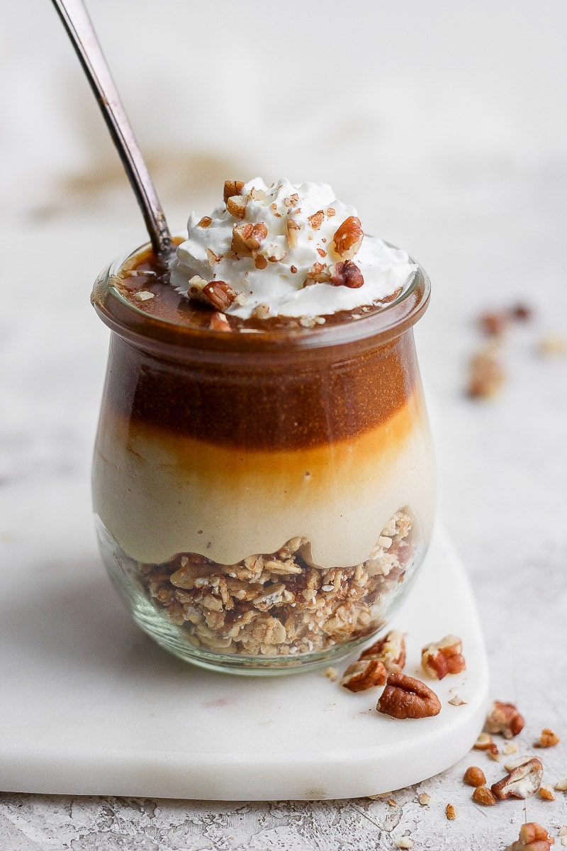 A vegan caramel cheesecake jar topped with whipped cream and pecans.