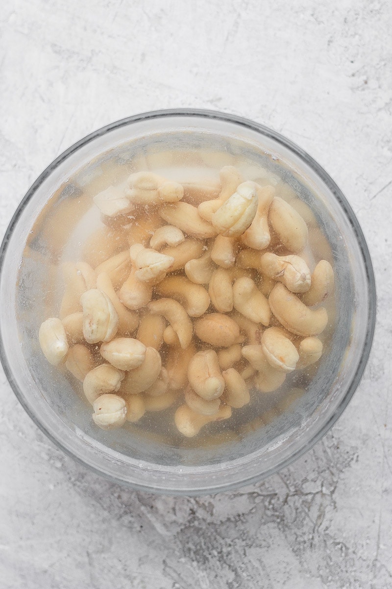 Raw cashews soaking in a glass bowl of hot water.