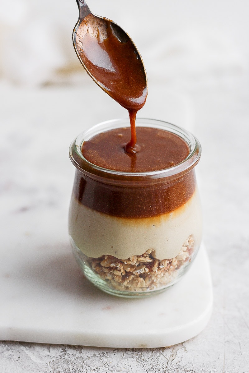 Caramel being poured on top of a mini cheesecake jar.
