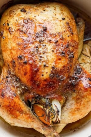 Top shot of a whole roasted chicken in a Dutch oven with a head of garlic next to it.