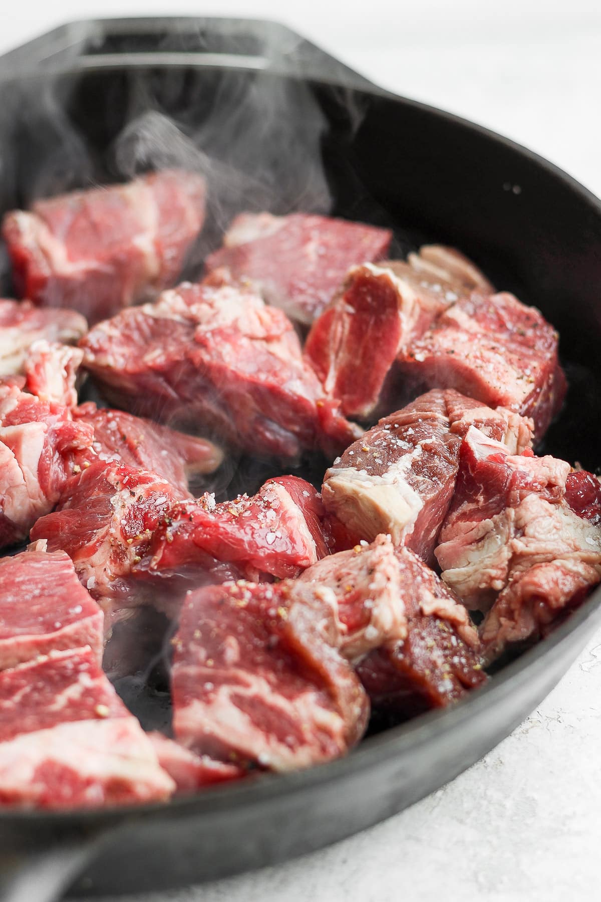 Beef chunks being seared in a cast iron skillet.
