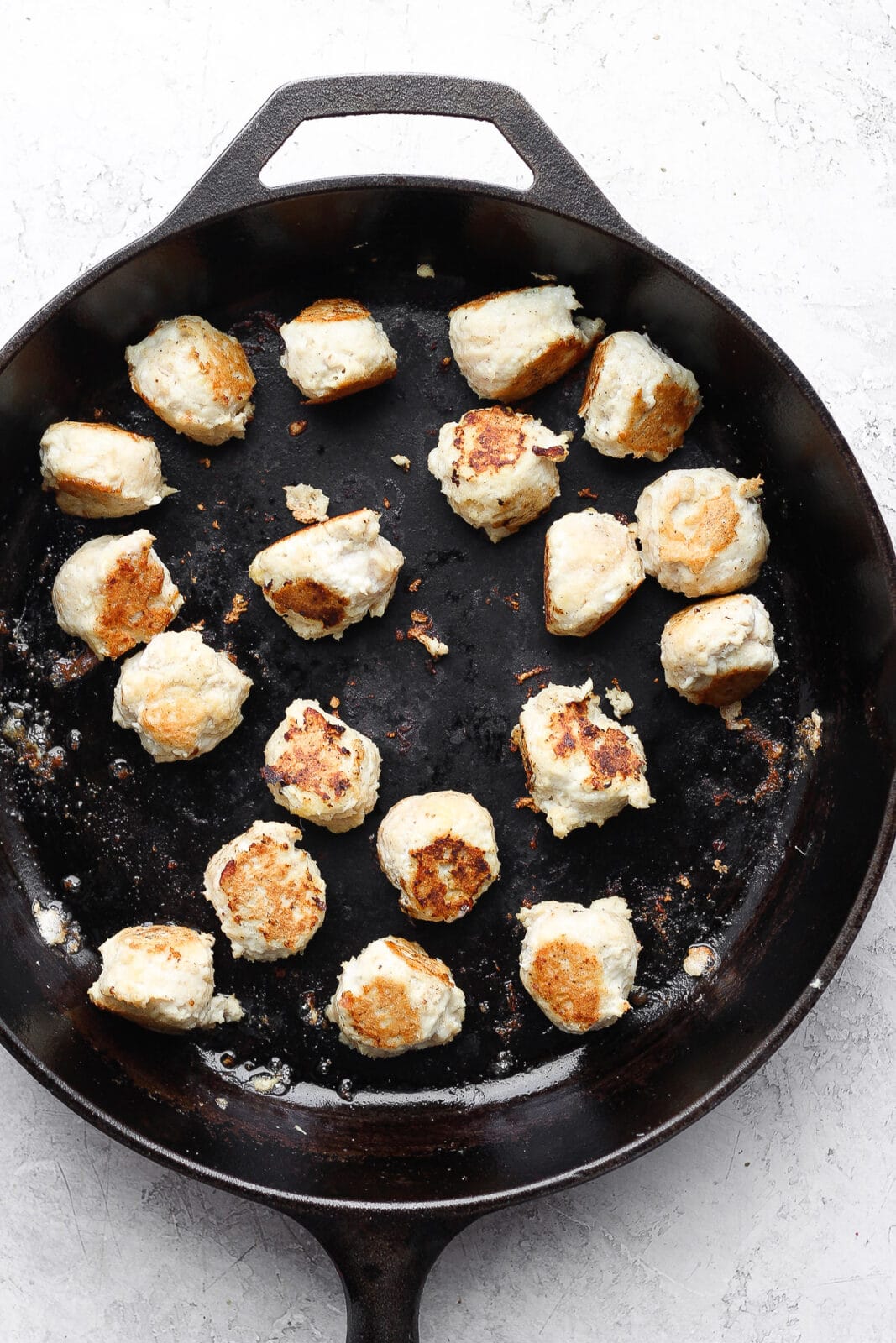 Large cast iron skillet with cooked chicken meatballs. 