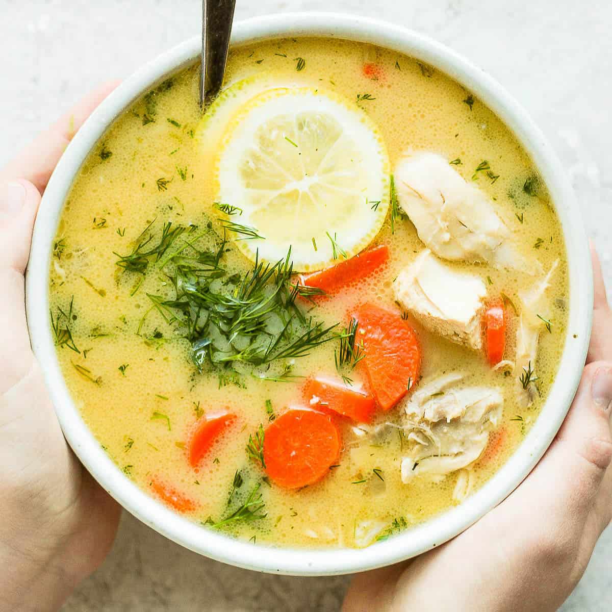 Two hands holding a bowl of Greek Lemon Chicken Soup.