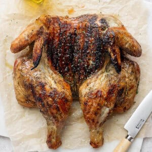 Top down shot of a grilled spatchcock chicken on a piece of brown parchment with a knife next to it.