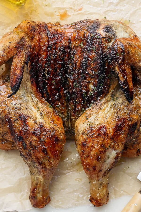 Top down shot of a grilled spatchcock chicken on a piece of brown parchment with a knife next to it.