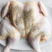A large white platter with a raw spatchcocked chicken that has been seasoned.