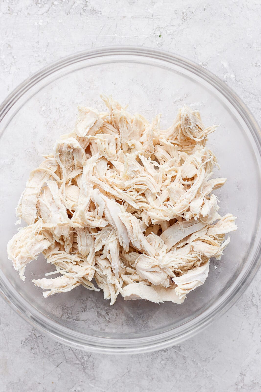 Glass bowl filled with cooked, shredded chicken. 