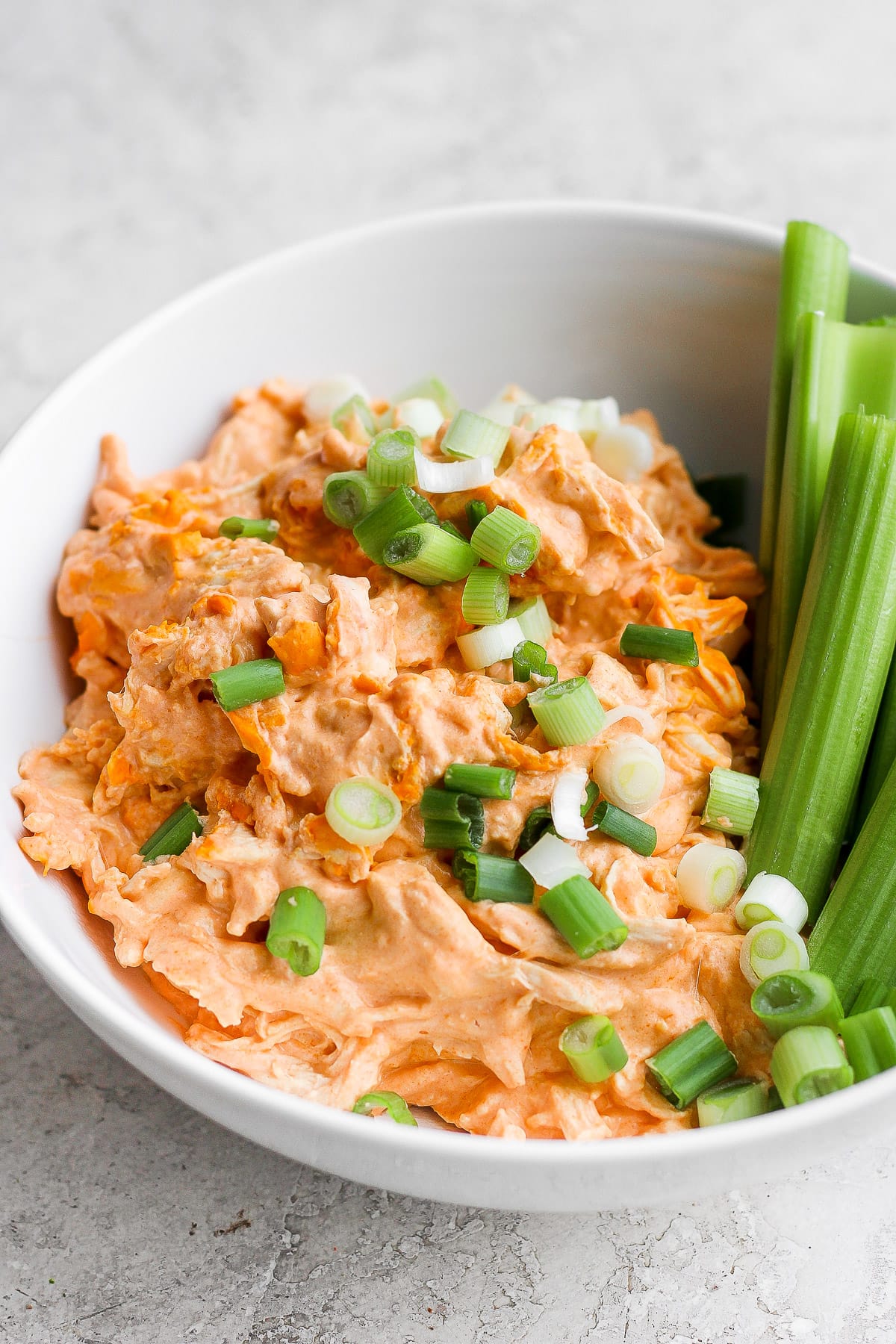 Bowl of healthy buffalo chicken dip with celery and chopped green onion. 