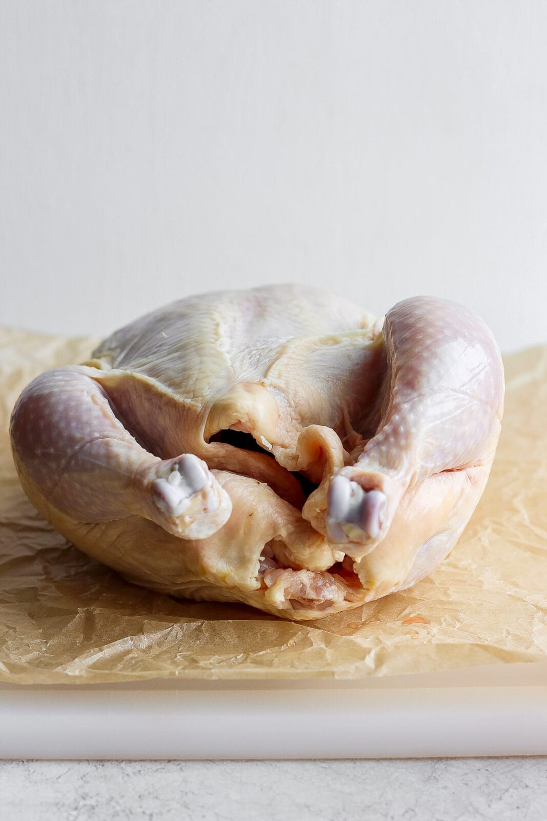 A whole, raw chicken sitting on parchment paper. 
