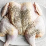 A spatchcocked chicken on a platter with seasonings on top of it.