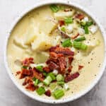 A bowl of loaded baked potato soup with bacon and green onion on top.