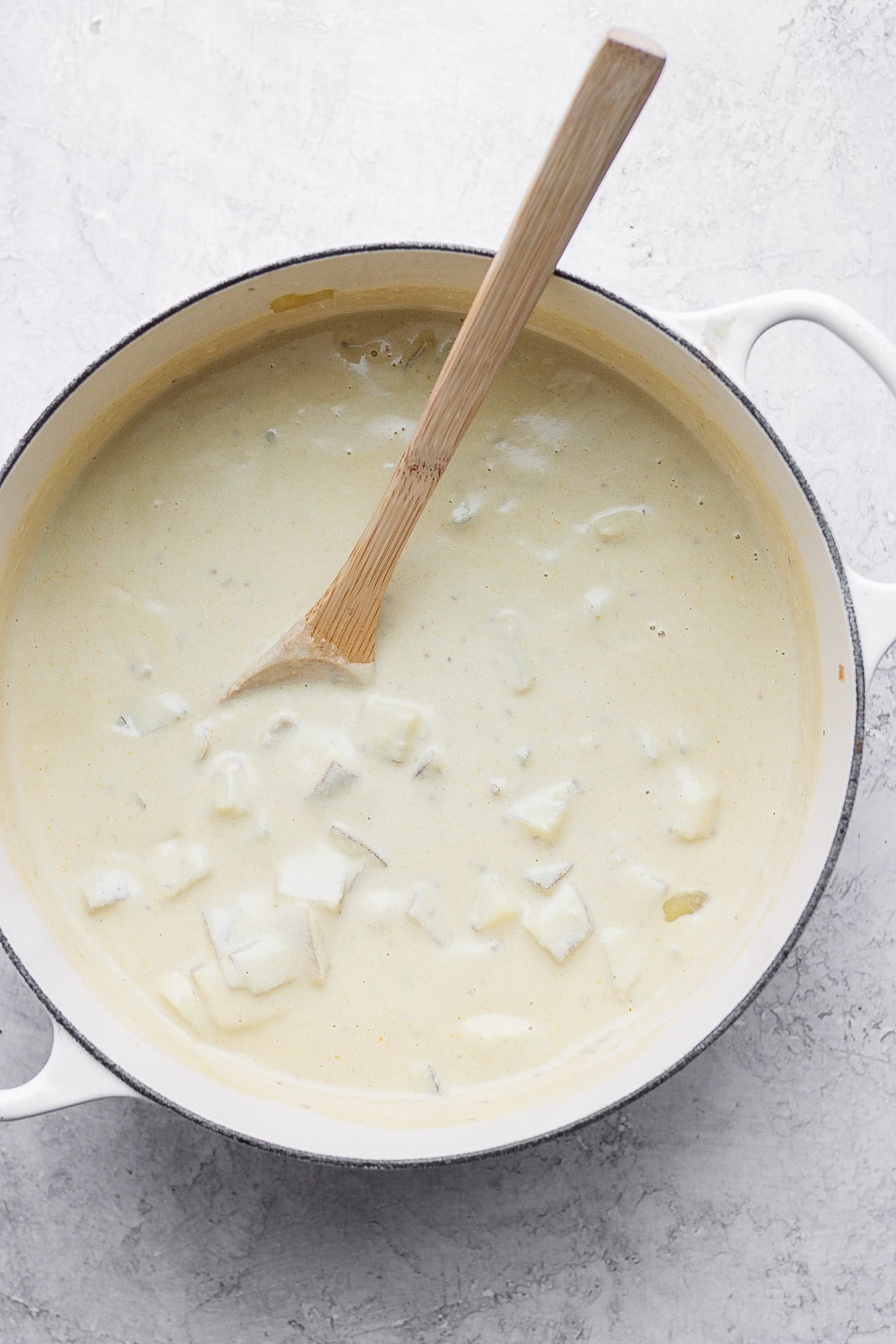 A dutch oven filled with baked potato soup and a wooden spoon sticking out of it.