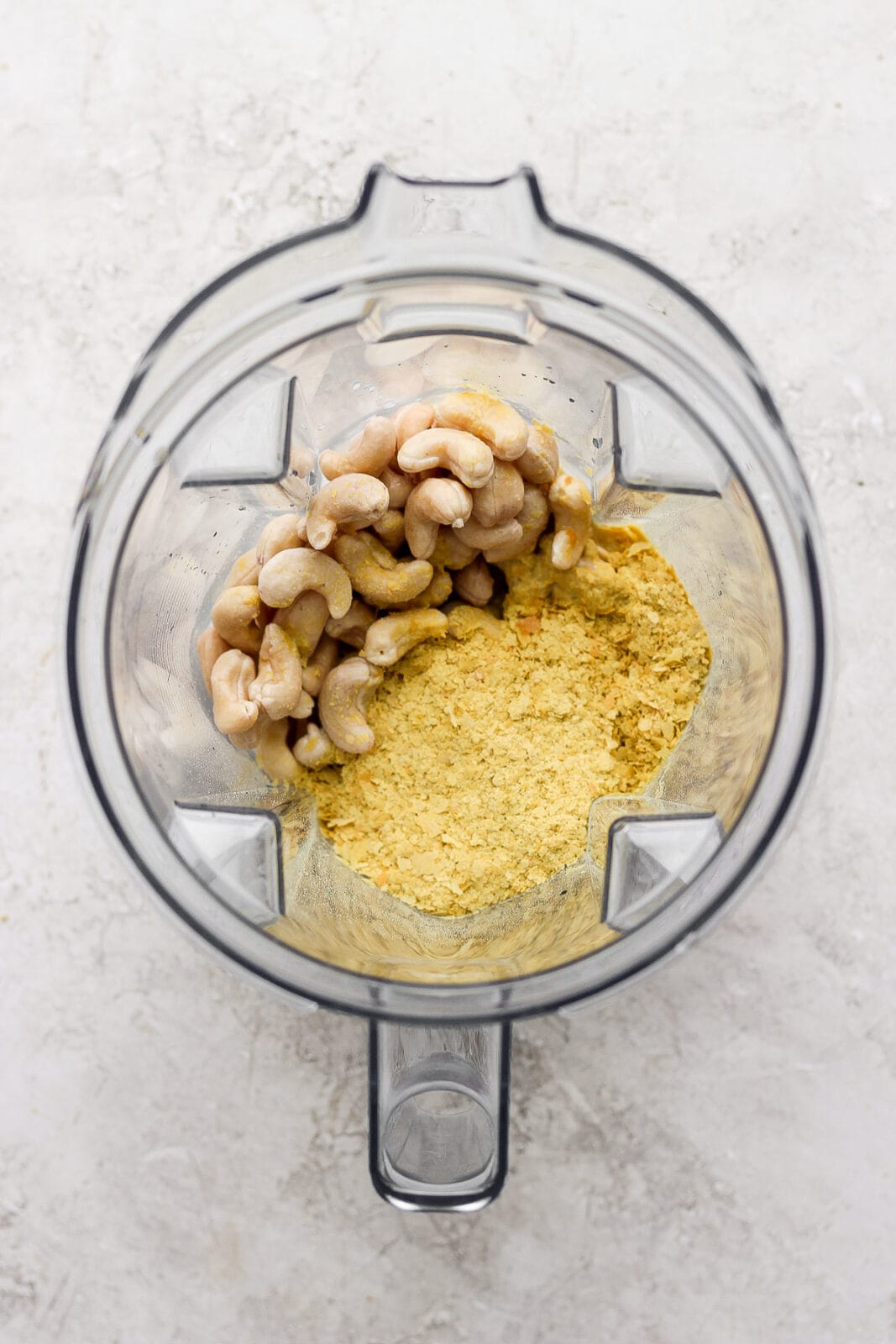 Top shot of blender filled with drained cashews and nutritional yeast.