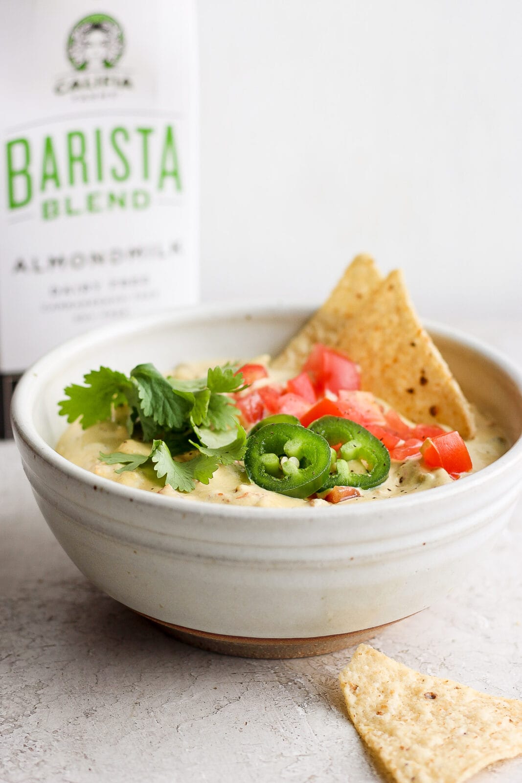 Bowl of vegan queso dip topped with fresh tomato, japaleno and cilantro. 