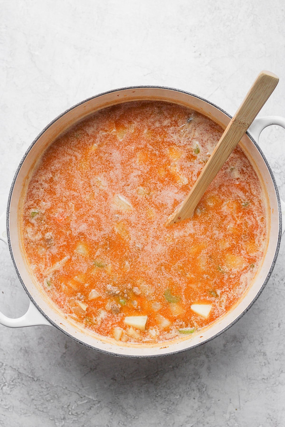 Broth added to the Dutch Oven and wooden spoon sticking out.