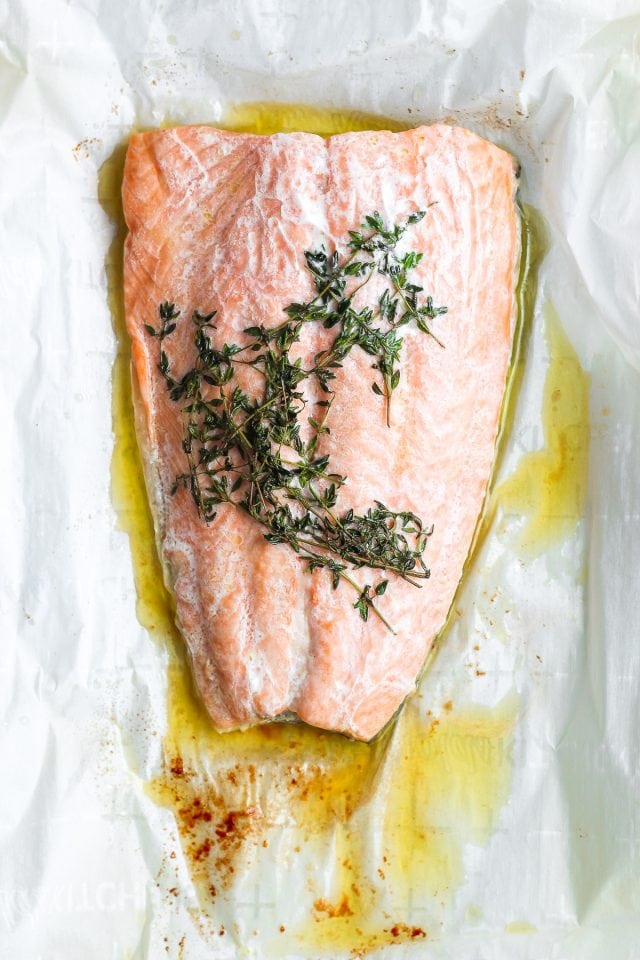 Parchment paper with a cooked fillet of salmon, melted ghee, and thyme.