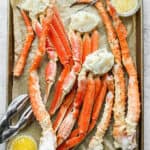 Top down shot of a baking sheet filled with baked crab legs and clarified butter.