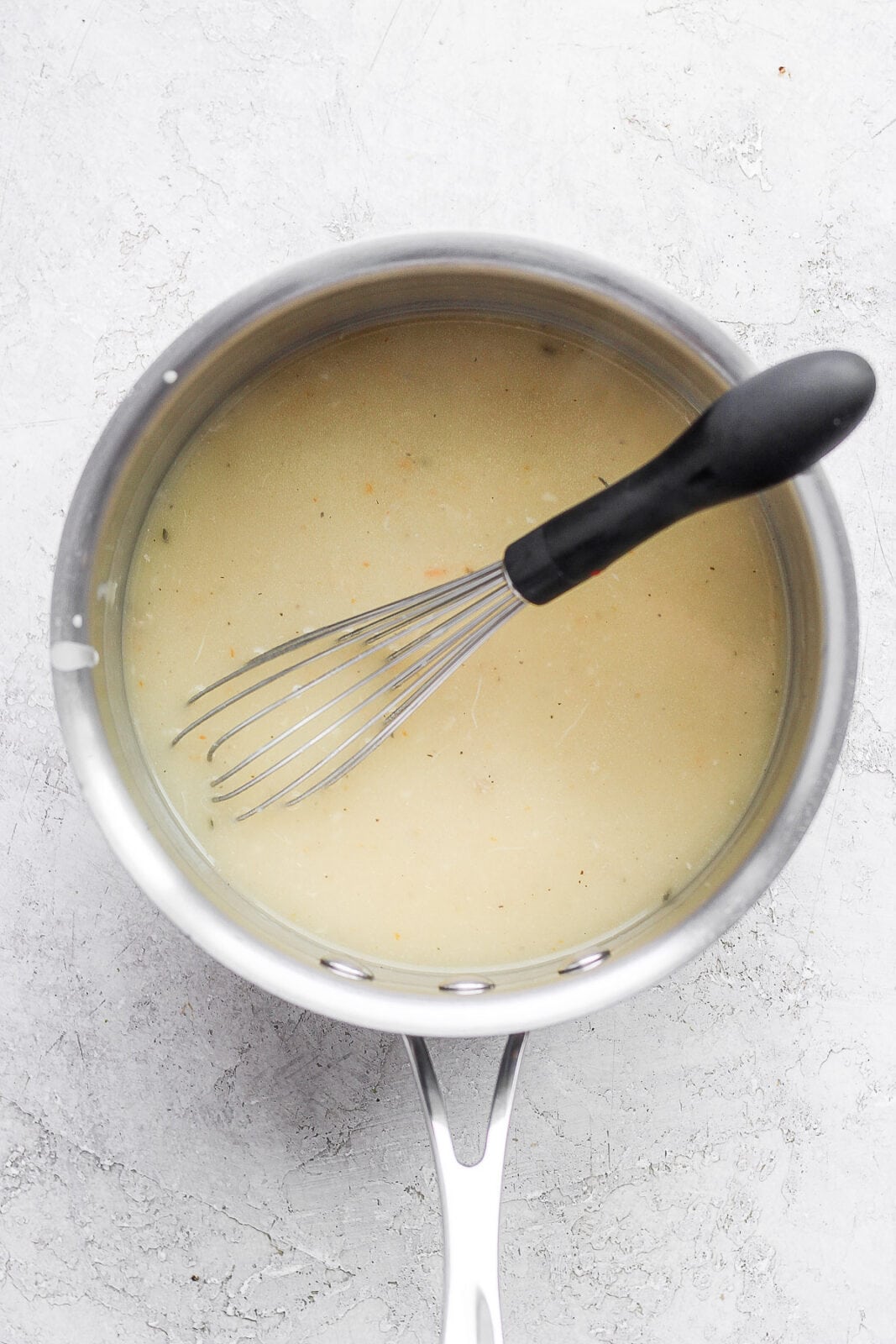 Saucepan filled with gravy with a whisk sticking out. 