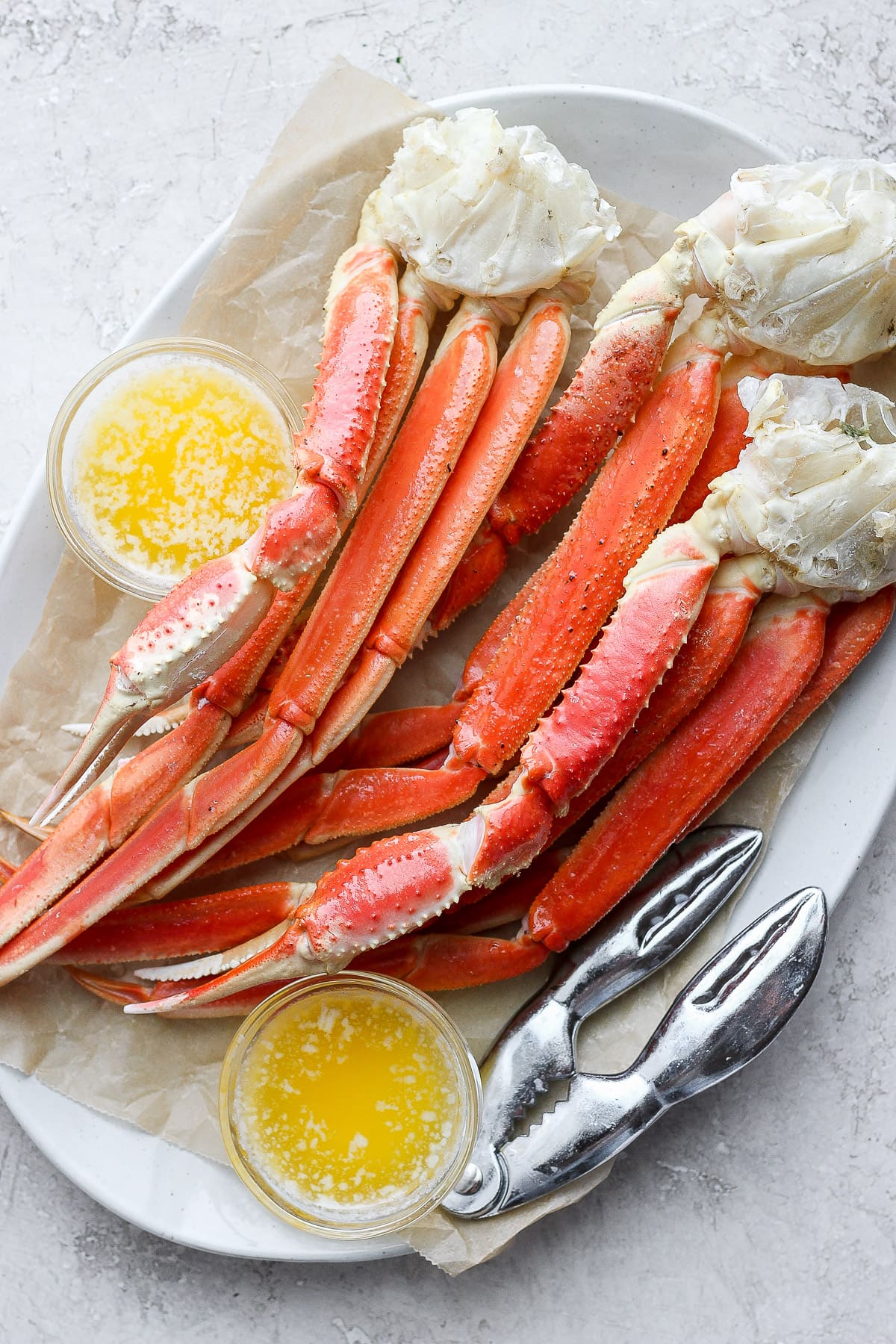 Plate of baked crab legs with little bowls of ghee next to them. 