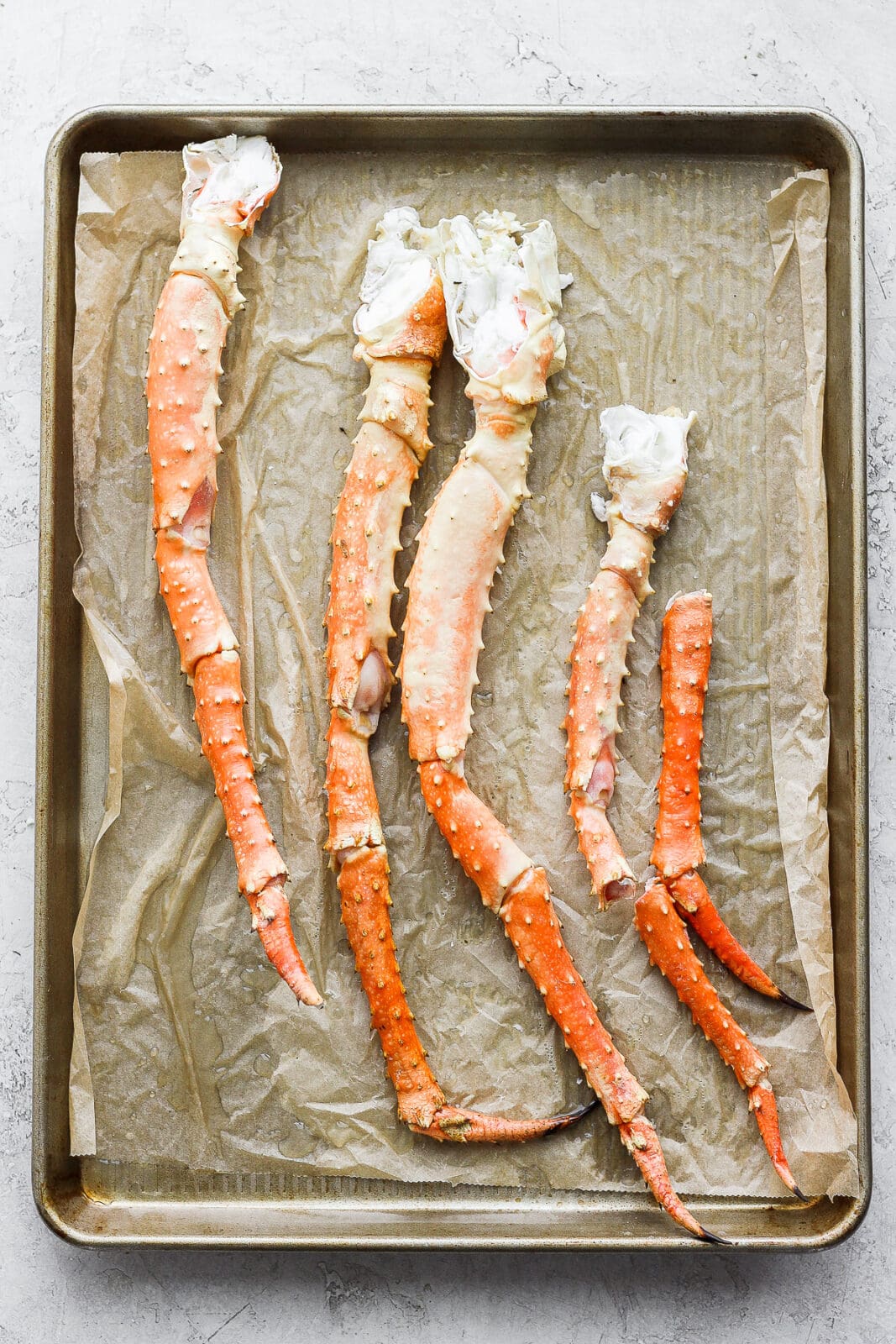 Parchment paper lined baking sheet with king crab legs on top.