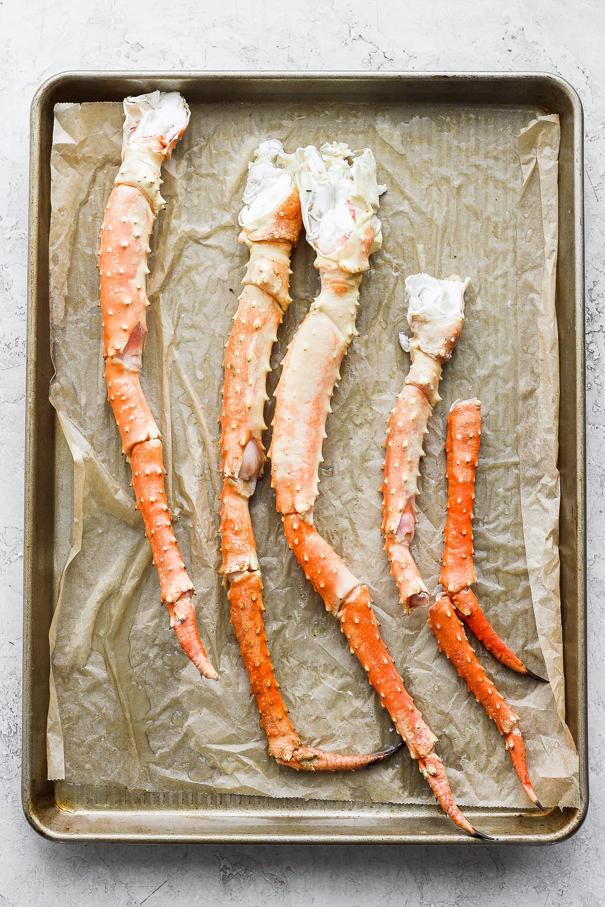 Parchment paper lined baking sheet with king crab legs on top. 