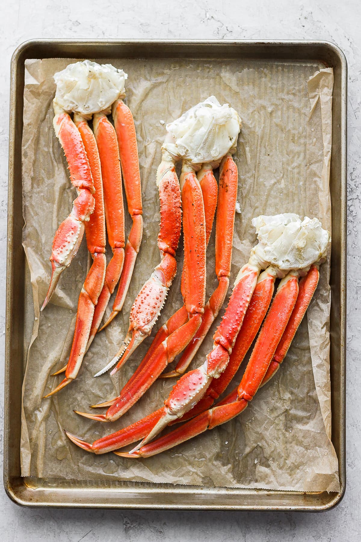 Parchment lined baking sheet with show crab clusters on top. 