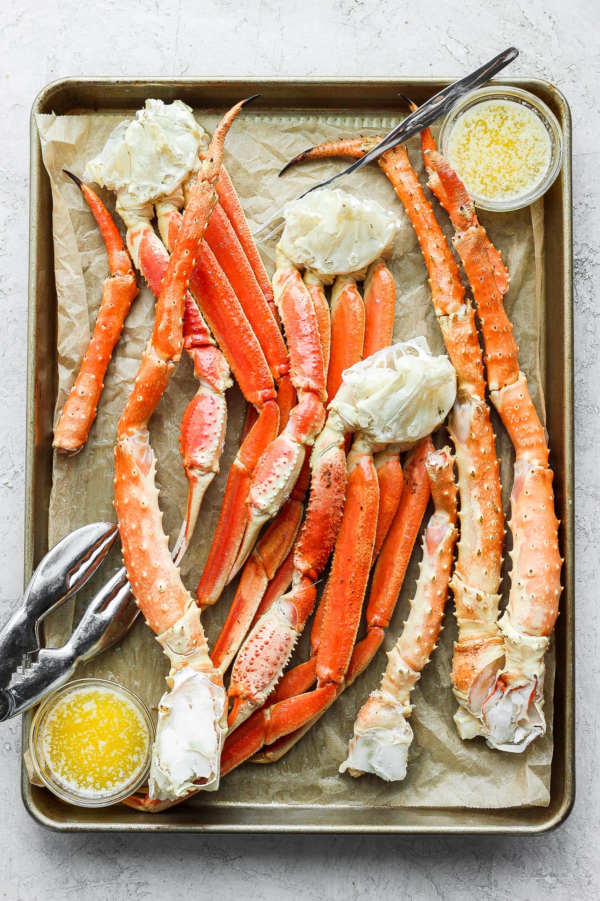 Parchment lined baking sheet filled with show crab and king crab legs as well as some bowls of ghee. 