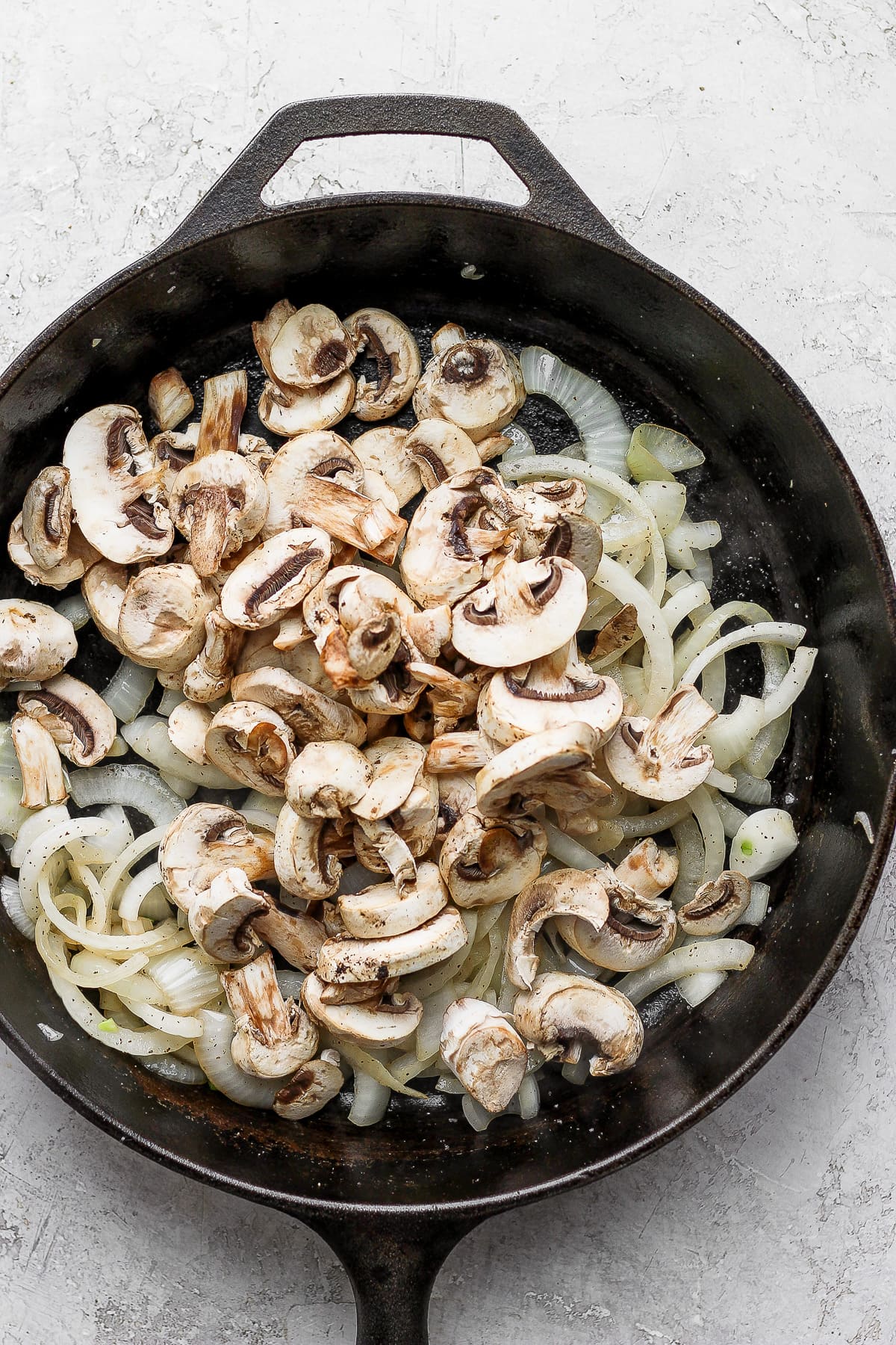 Cast iron pan with slightly cooked onions and sliced mushrooms.