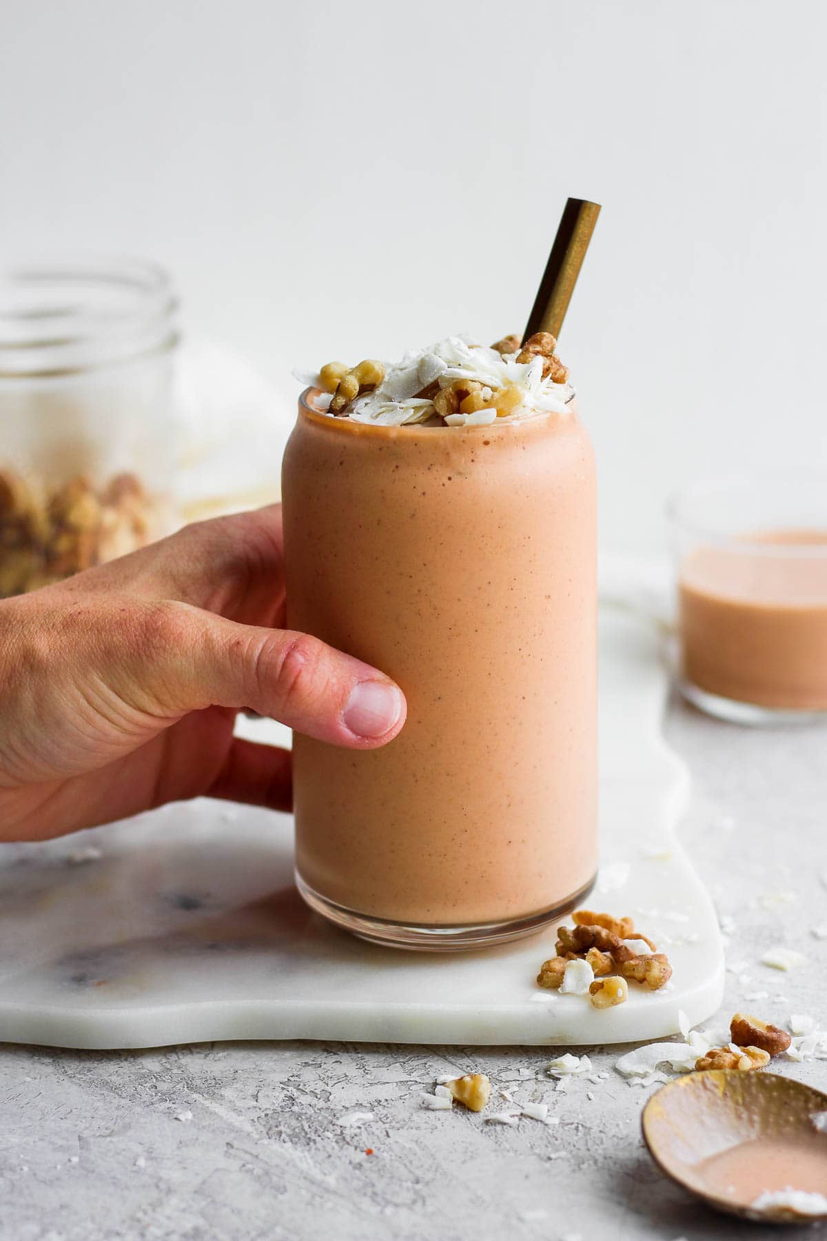 A carrot cake smoothie on a white board with a hand grabbing it. 