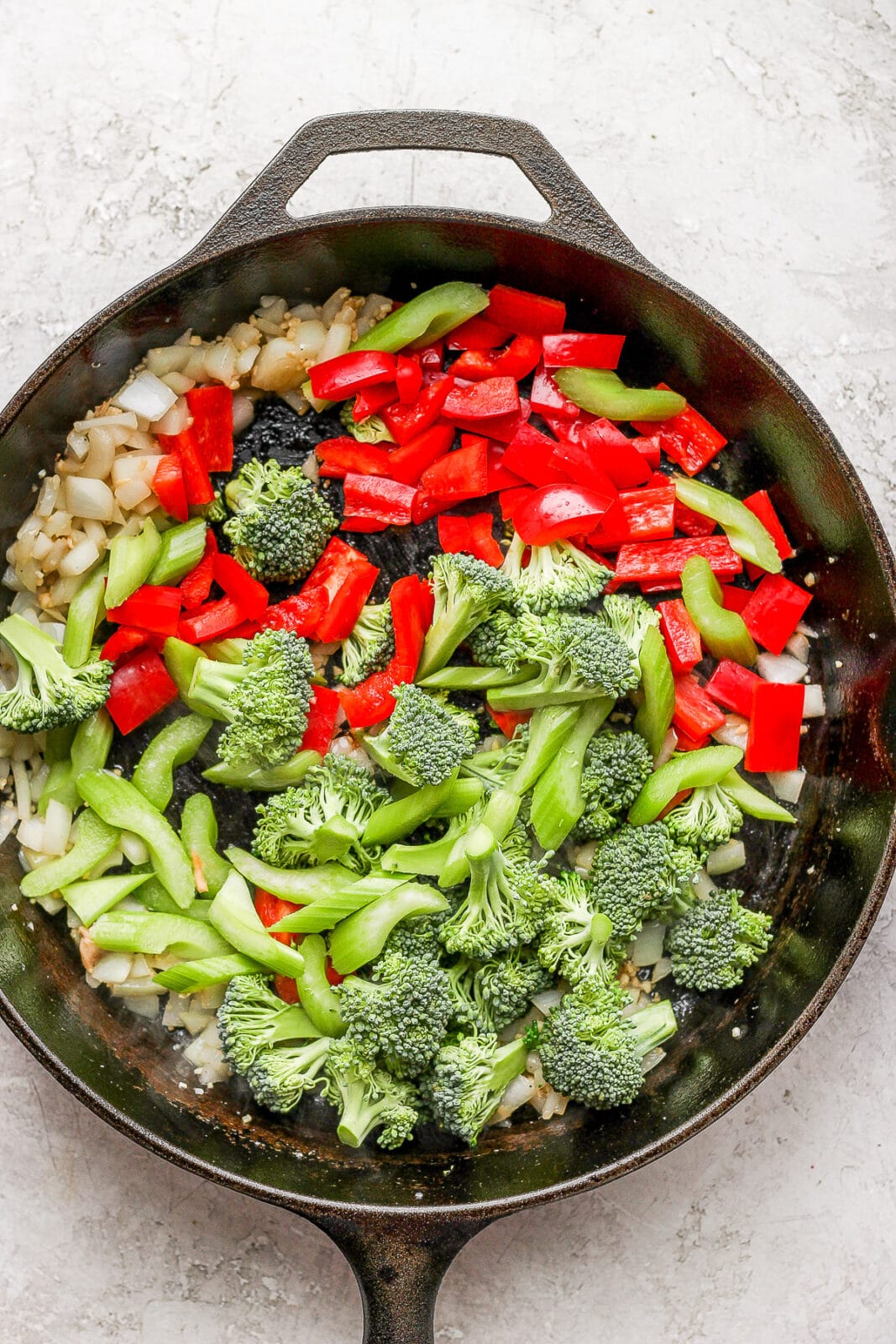 Cast iron pan with cooked garlic & ginger plus broccoli, celery, and red bell pepper.