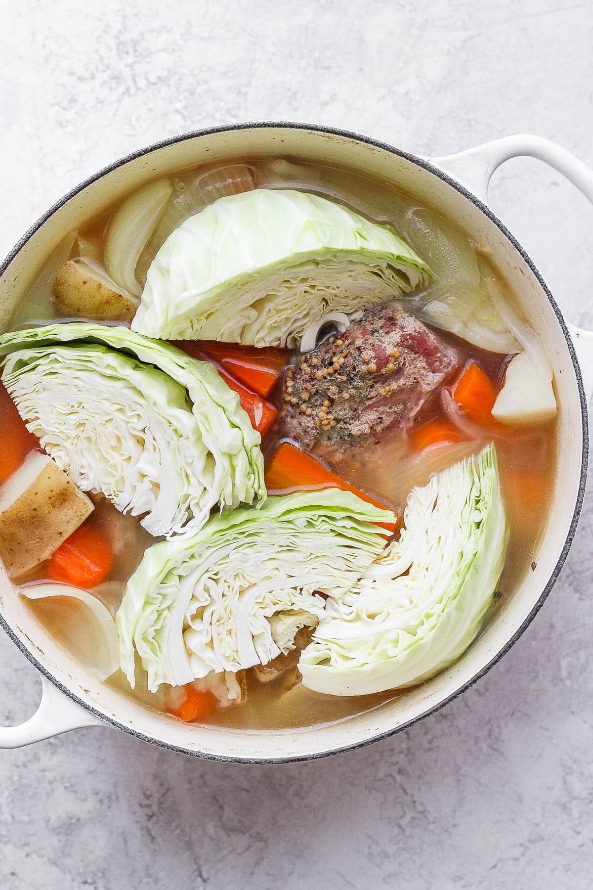 Dutch oven filled with a cooked corned beef and raw cabbage on top. 