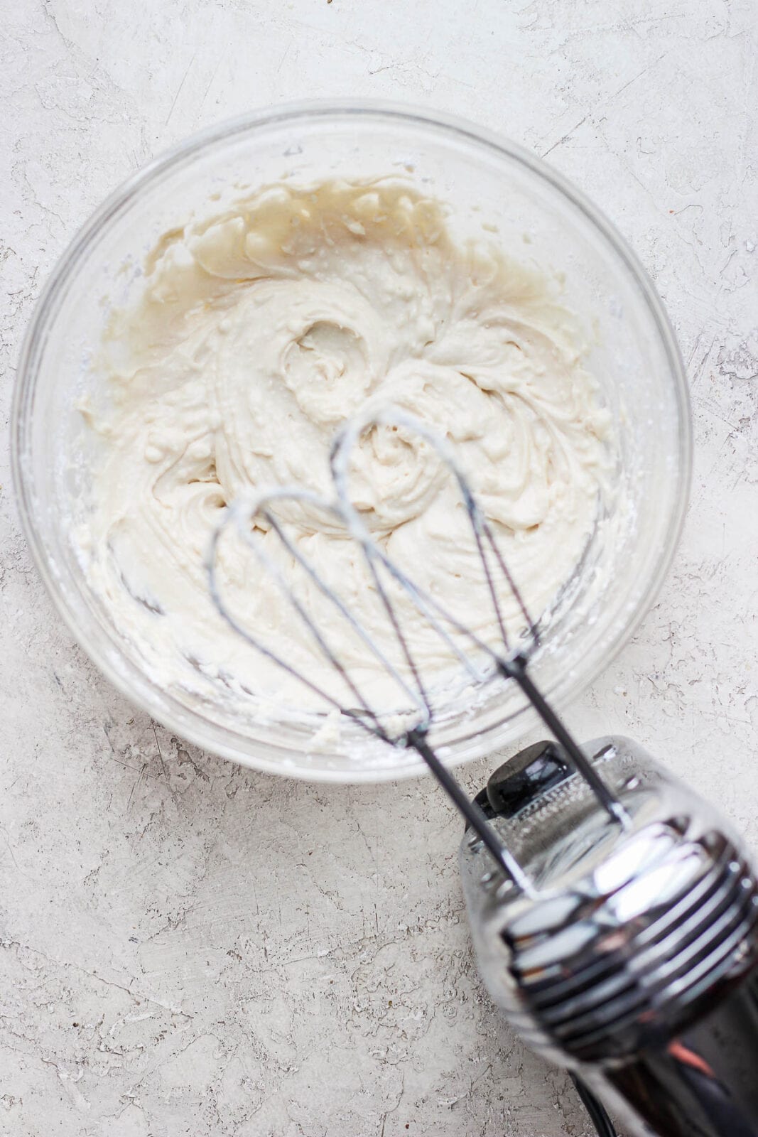 Bowl of dairy free cream cheese and vegan butter being mixed together with a hand mixer.