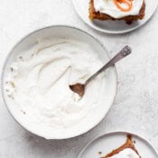 A bowl of dairy free cream cheese frosting with two plates of carrot cake next to it.