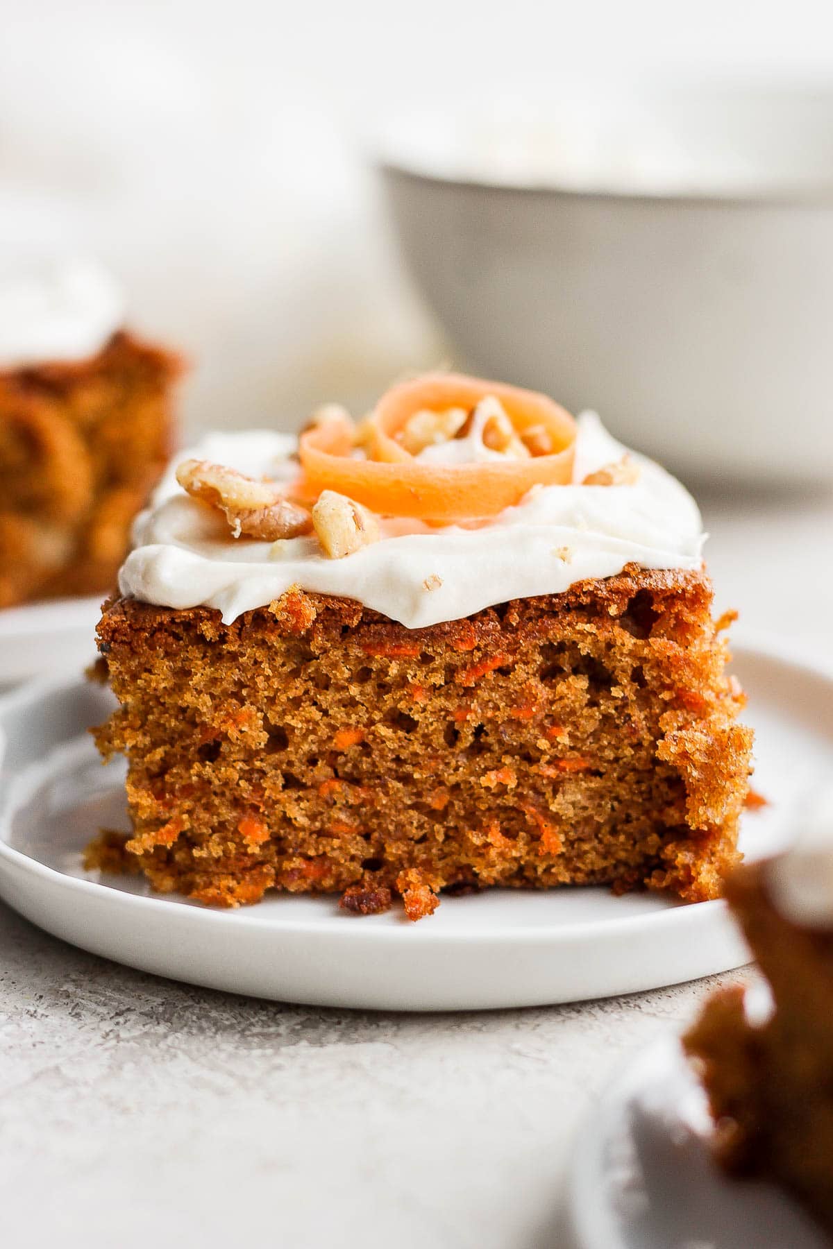 Slice of gluten free carrot cake on a plate with cream cheese frosting.
