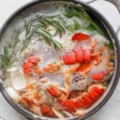 A stockpot of seafood stock being made with lobster tails and fresh herbs.