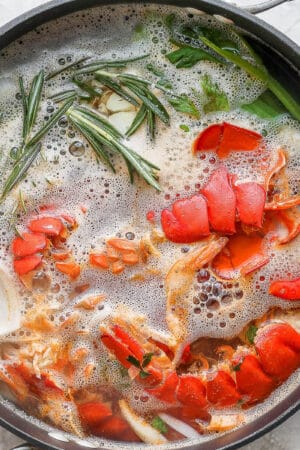 A stockpot of seafood stock being made with lobster tails and fresh herbs.