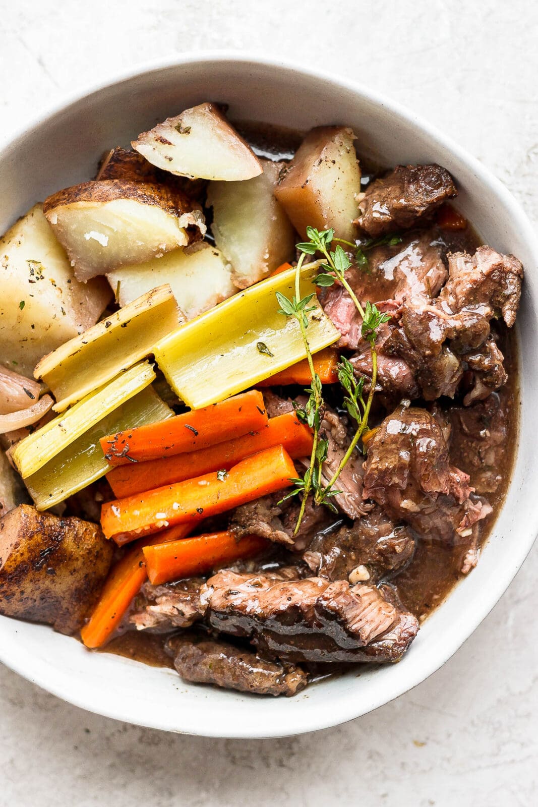 Bowl of cooked slow cooker pot roast with vegetables and gravy.