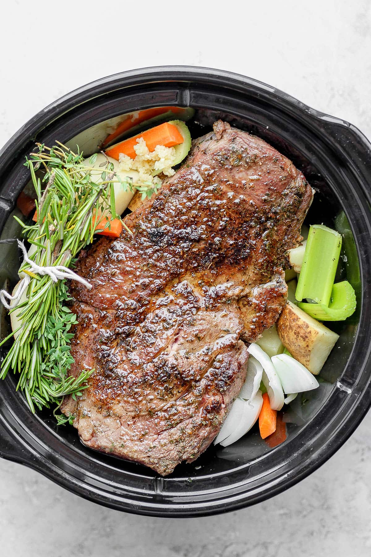 Slow cooker with beef roast, vegetables, and herbs.