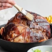 A smoked ham in a cast iron skillet getting brushed with the juices.