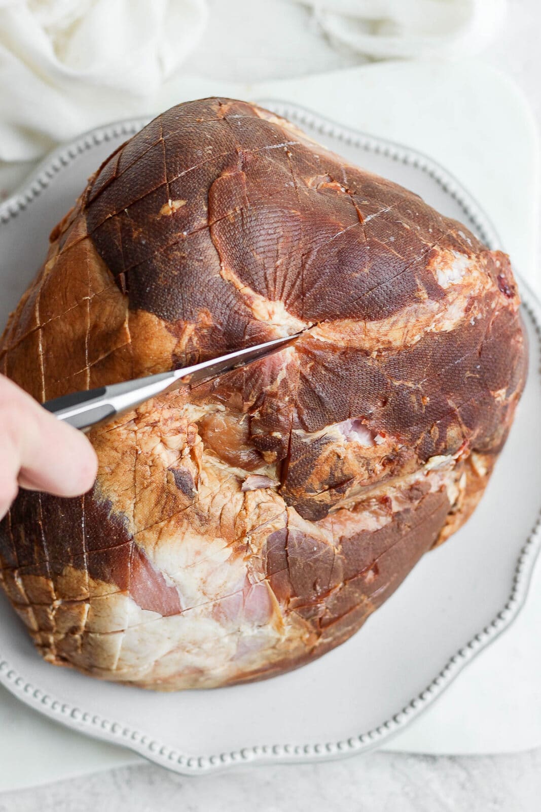 Scoring a ham with a knife on a plate.