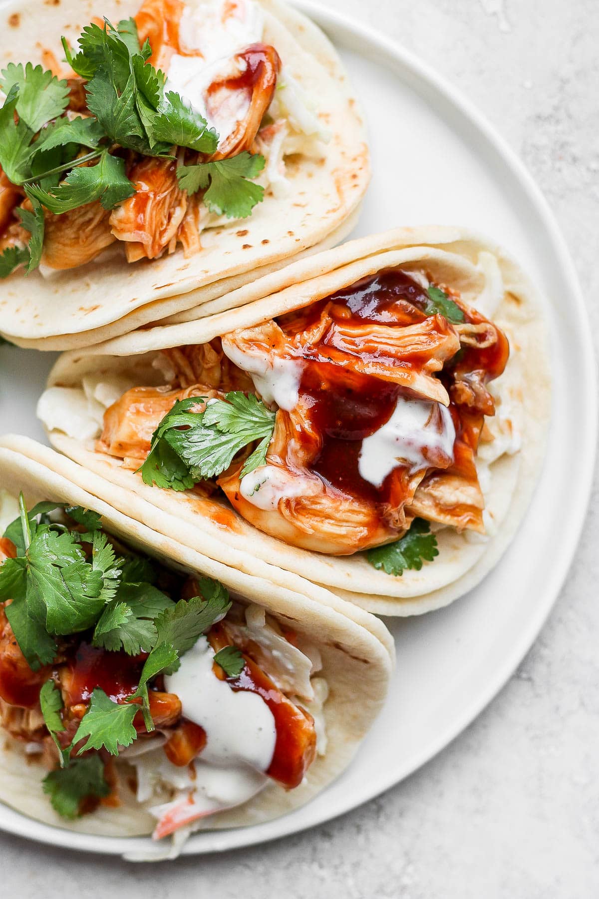 A plate with 3 BBQ chicken tacos and some coleslaw on top.