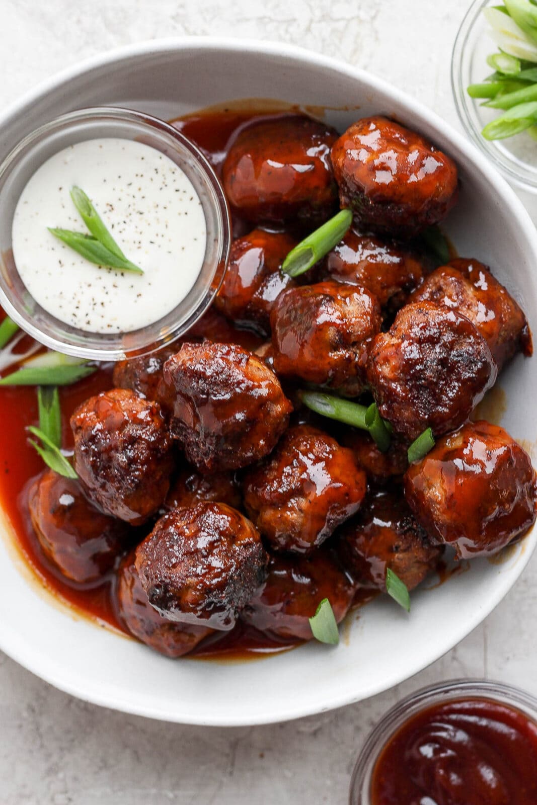 Bowl of BBQ meatballs, sliced green onions, and dipping sauce.