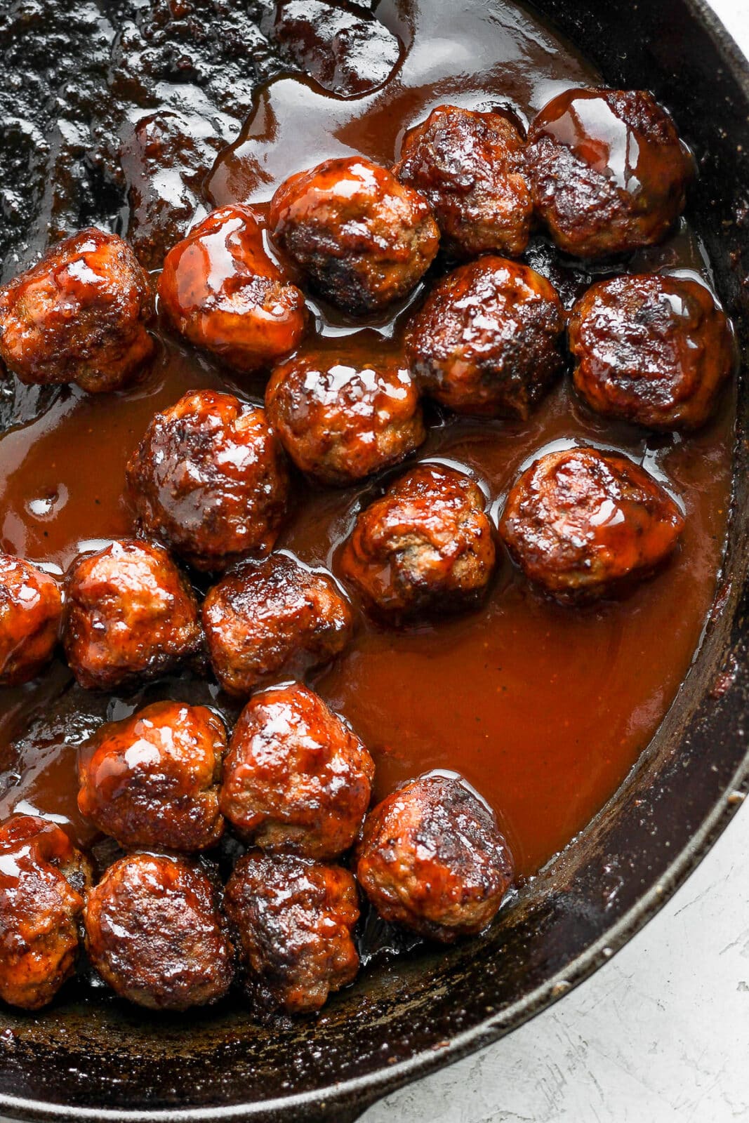 Cast iron skillet with cooked meatballs and BBQ sauce.