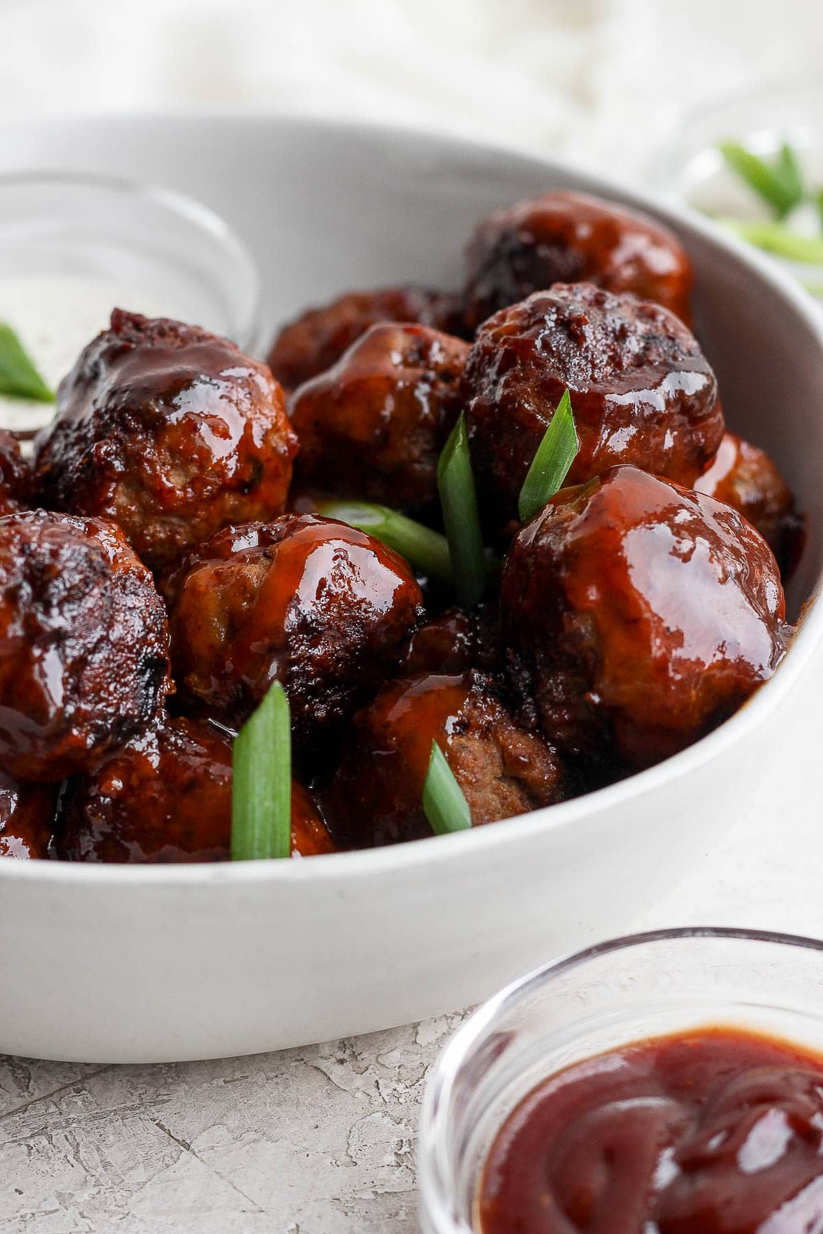 Bowl of BBQ meatballs with sliced green onions and dipping sauce.
