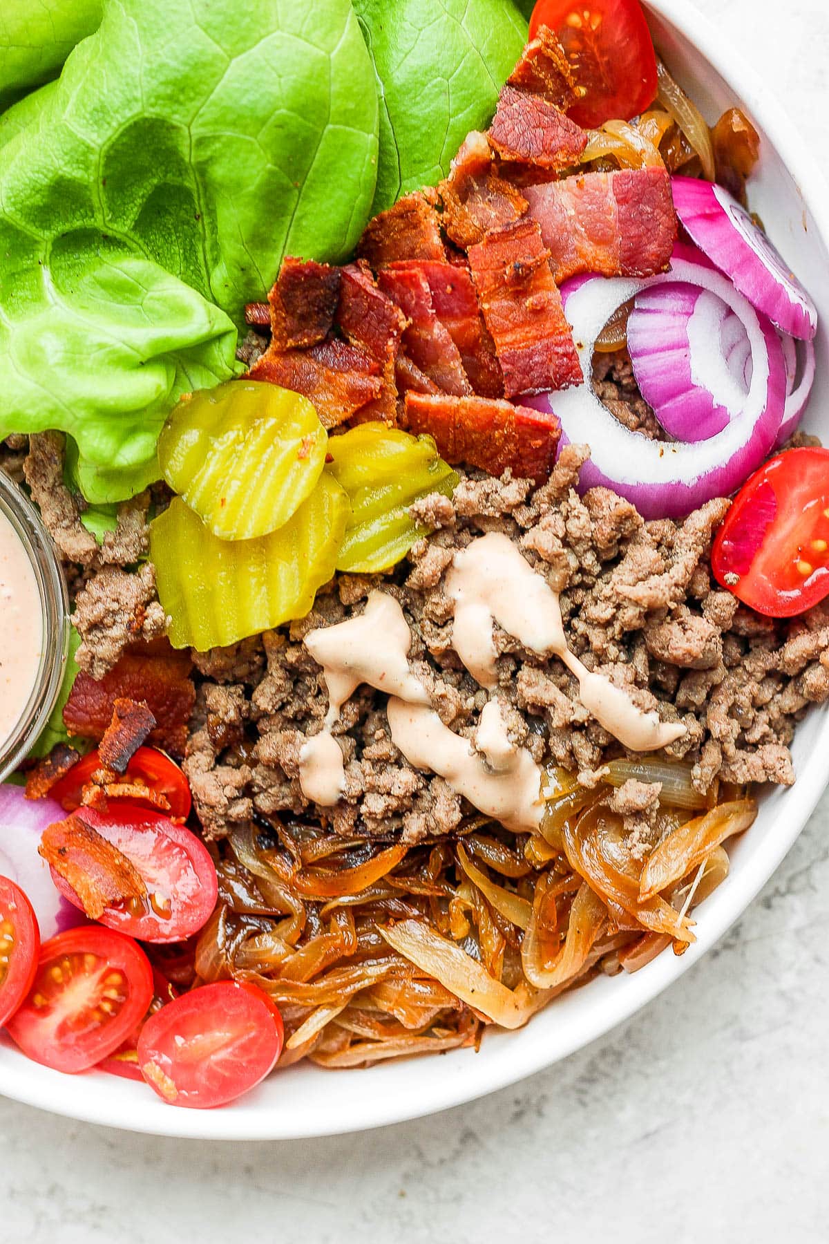 All burger bowl ingredients in a bowl with a small dish of burger sauce.