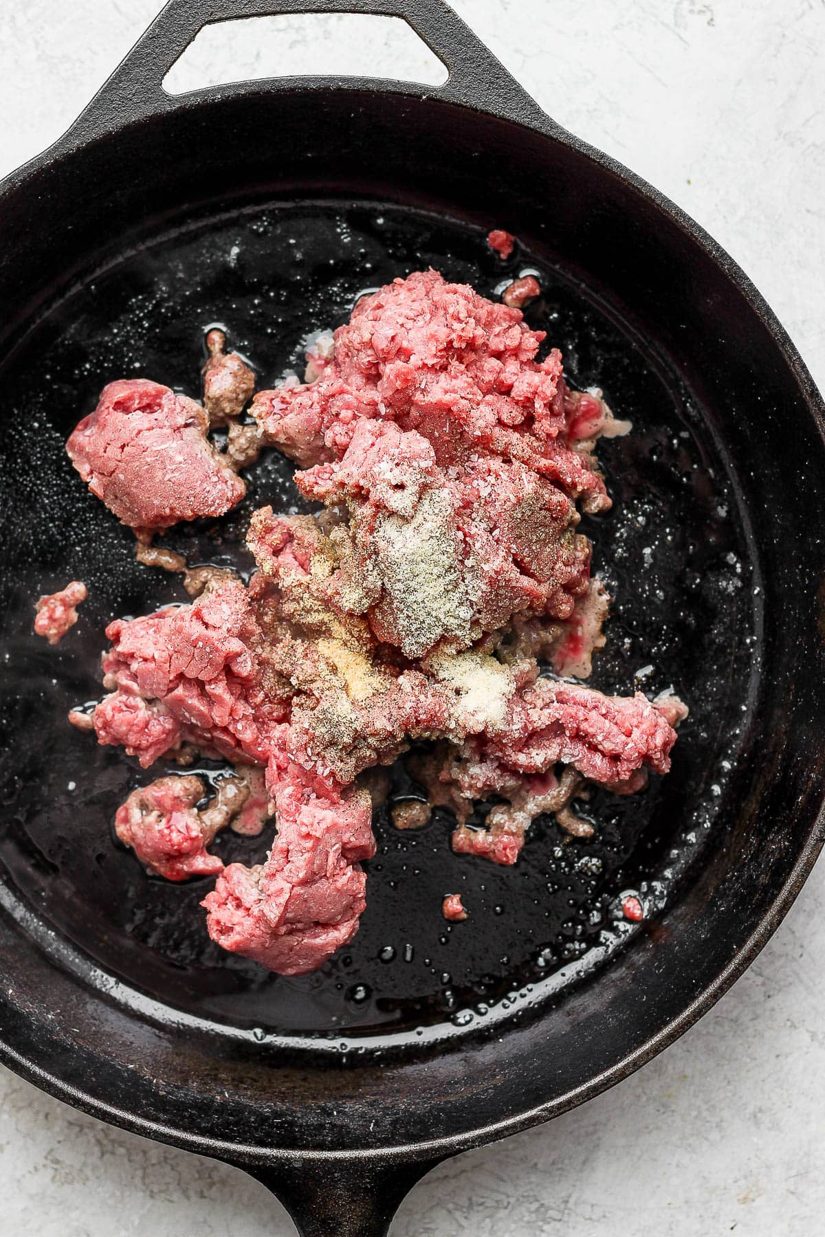 Ground beef with seasoning being browned in a cast iron pan.